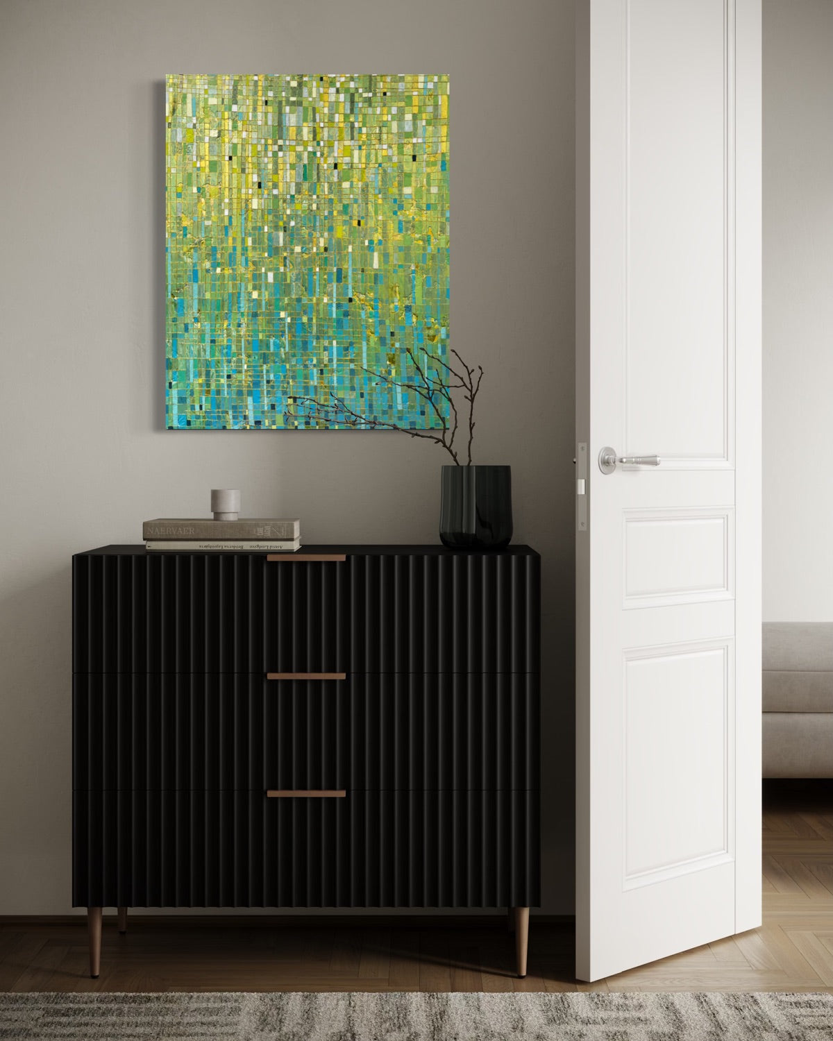 An abstract painting with a textured mosaic pattern in yellow, green, and blue hangs on a gray wall above a black ribbed console cabinet in a modern room setting.