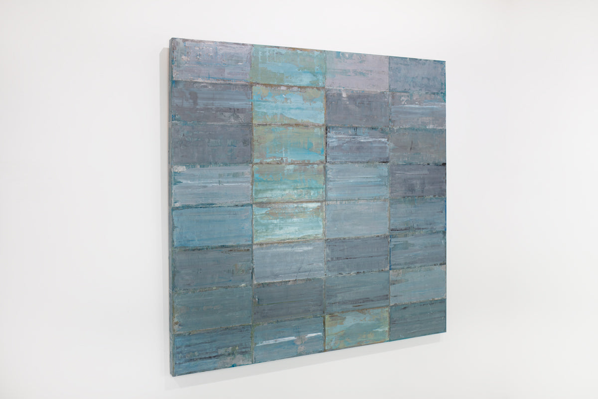 A blue and grey abstract geometric painting hangs on a white wall.