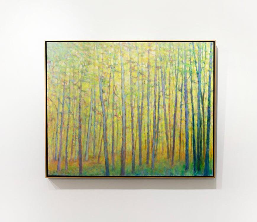 A yellow abstracted forest trees painting framed in a thin gold floater frame hangs on a white wall. 
