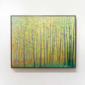 A yellow abstracted forest trees painting framed in a thin gold floater frame hangs on a white wall. 