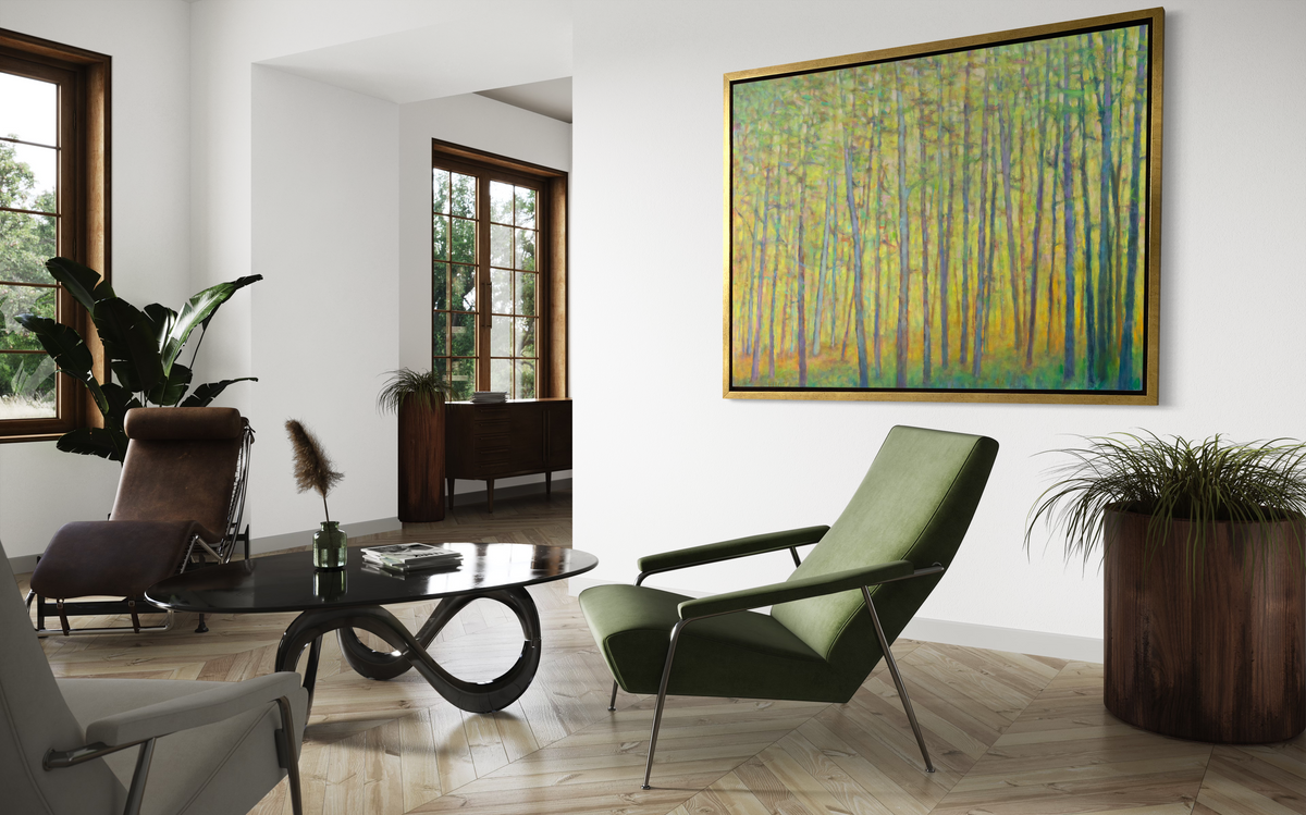 A side view of a green and yellow impressionist landscape print in a gold floater frame hangs on a white wall above a low green armchair, a modern black coffee table and some potted floor plants.