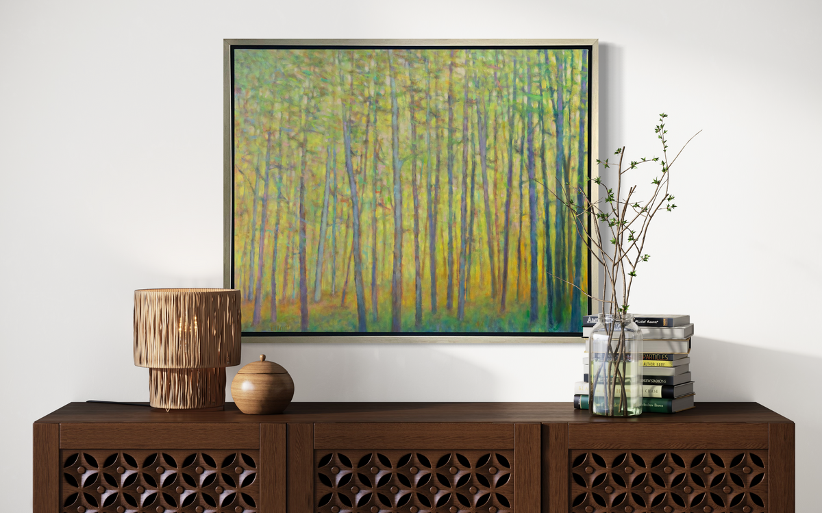 A green and yellow impressionist landscape print in a silver floater frame hangs on a white wall above a dark wood console cabinet with a stack of books, a clear jar with greenery stems and a straw light fixture.