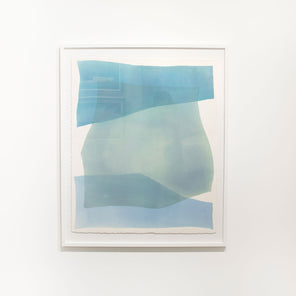 A framed blue abstract watercolor painting hangs on a white wall. 