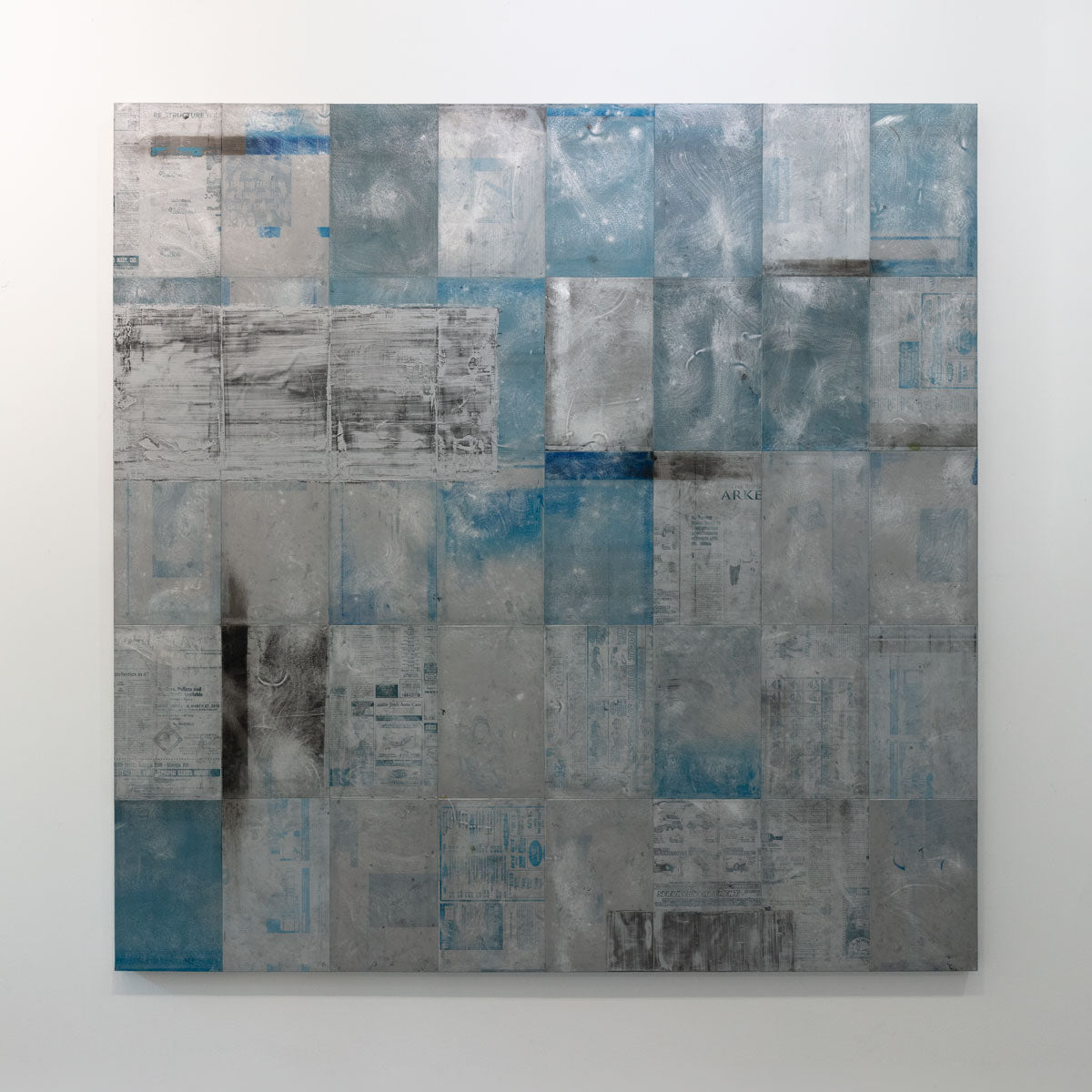 A blue painting on recycled metal print plates is hung on a gallery wall.