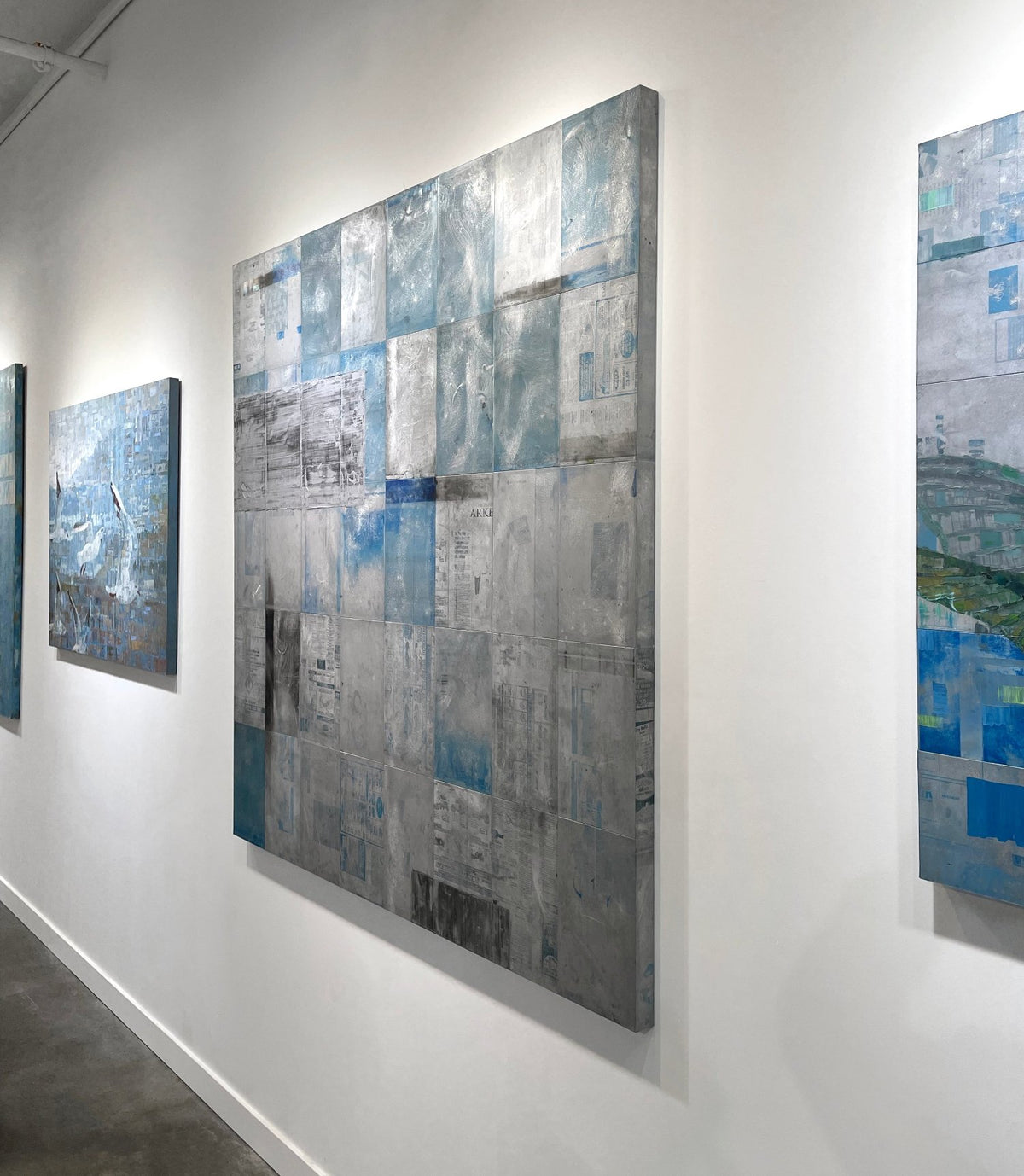 A blue painting on recycled metal print plates is seen at an angle on a gallery wall.
