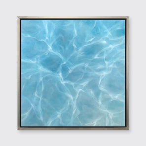 A tonal blue and white abstract seascape print in a silver floater frame hangs on a white wall.