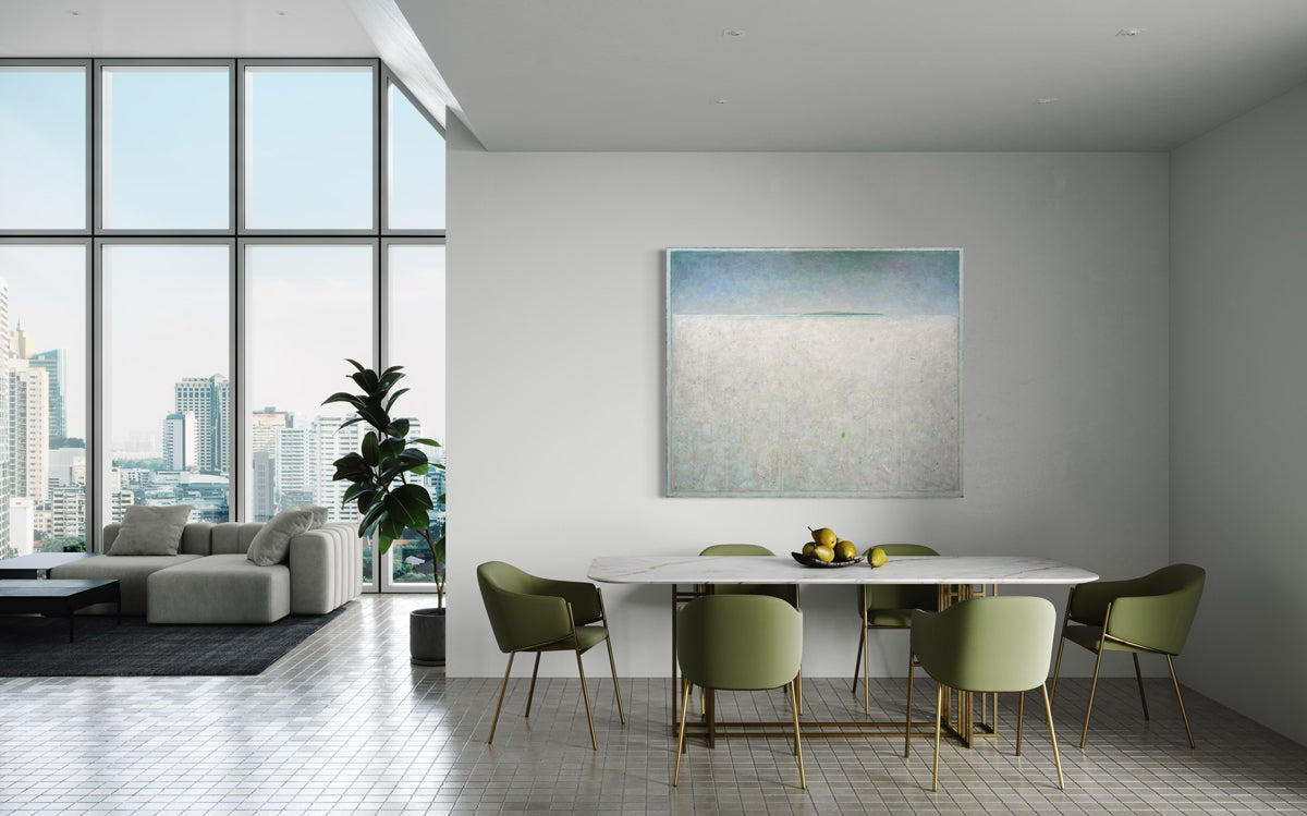 A white abstract landscape painting by Elwood Howell hangs on white wall over a dining table with green chairs.
