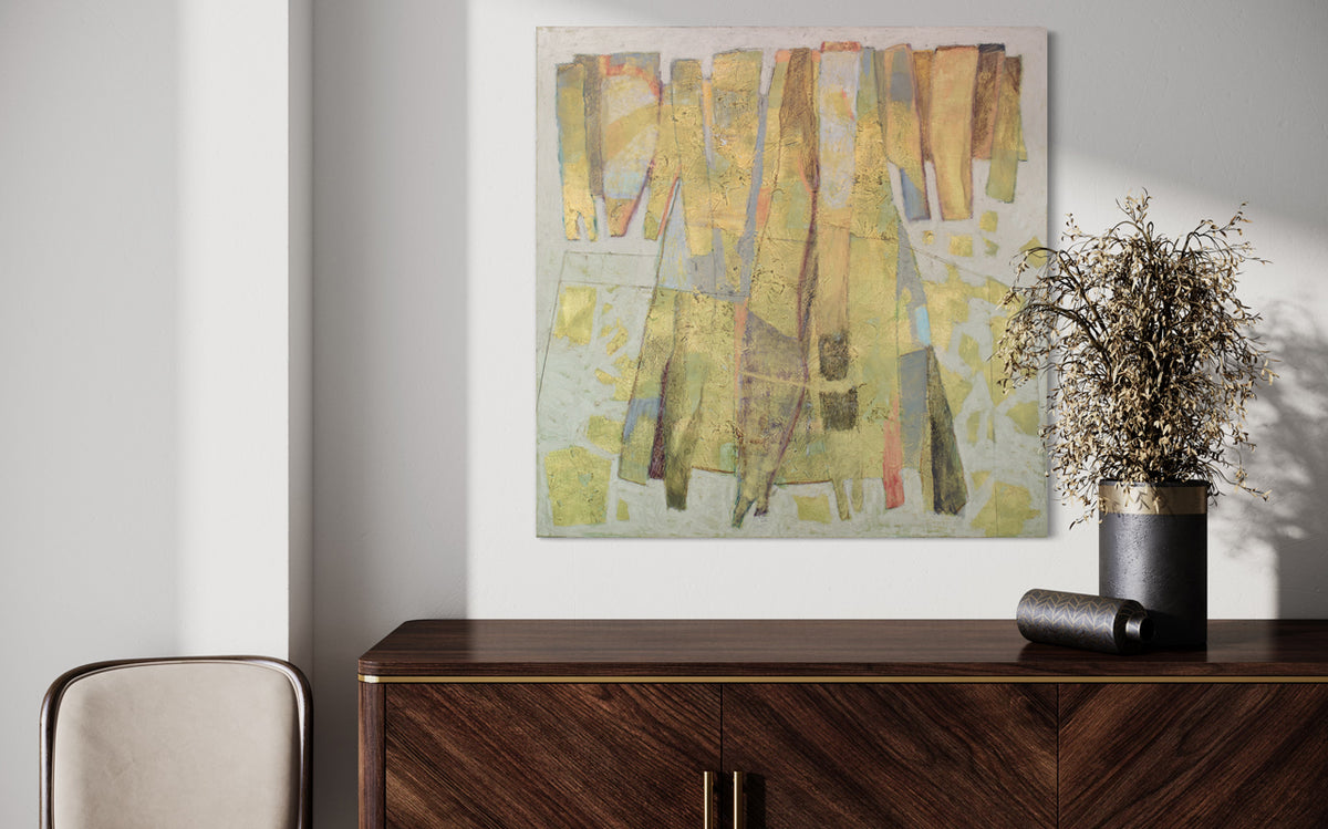 A metallic abstract painting hangs on a white wall above a midcentury modern console table with black vases with plants in them and light suede chair. 