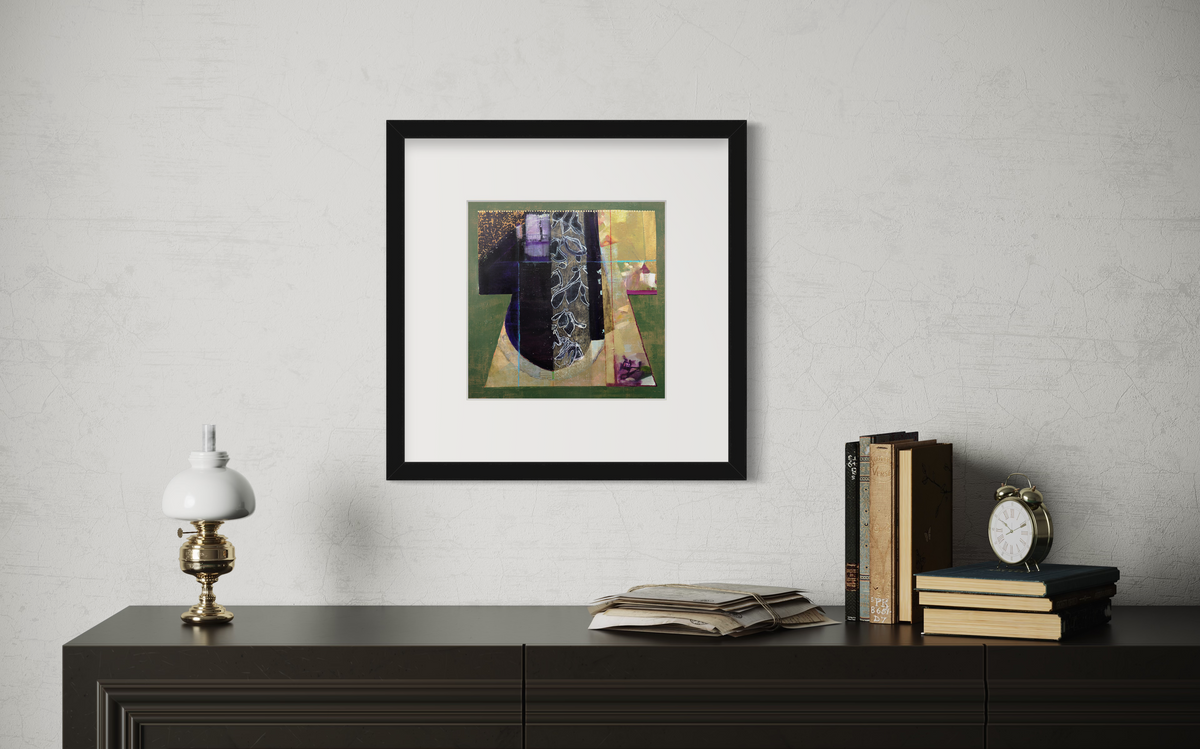 A green, gold and black abstract print in a black frame with a mat hangs on a white wall above a dark surface with stacks of books, a small lantern and a analog alarm clock.