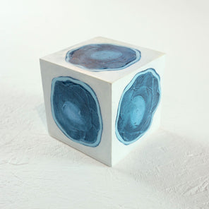 A white cube with a painted blue circle on each face rests on a white surface. 