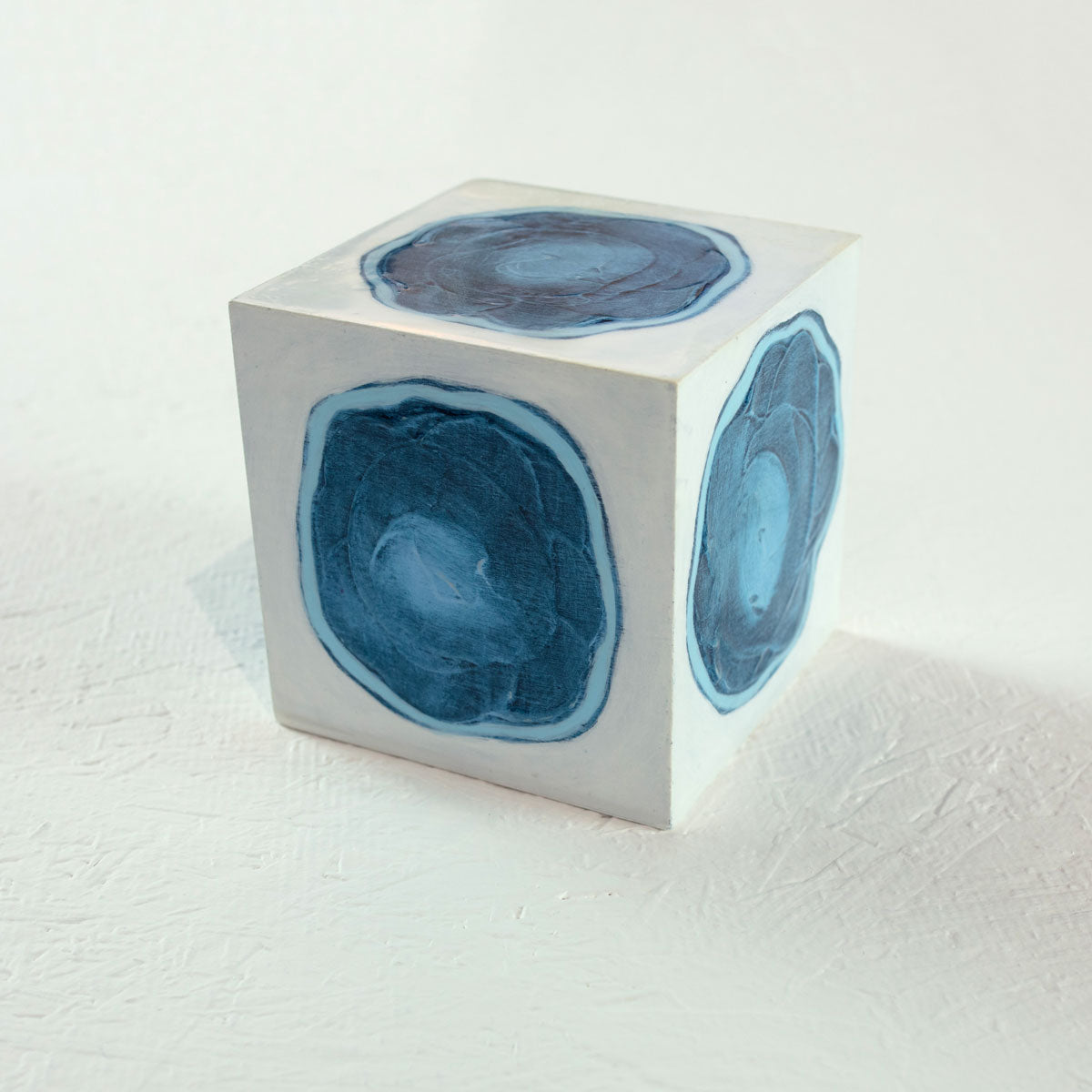A white cube with a painted blue circle on each face rests on a white surface.