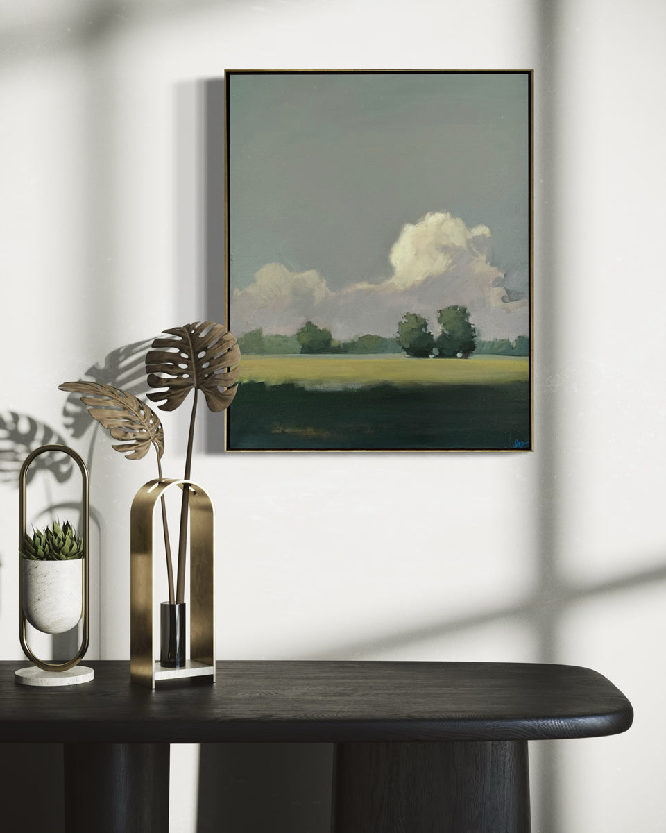 Framed landscape painting on a wall above a dark surface with decorative items.