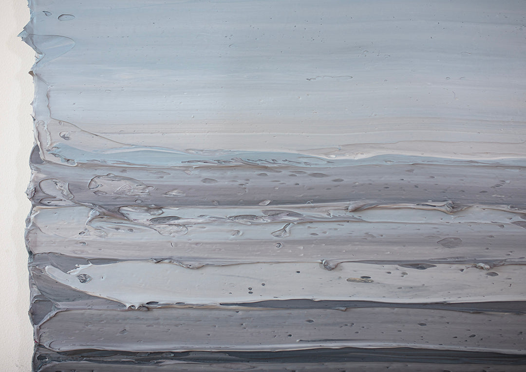 A dark grey blue, light blue, blue green, and white thickly textured detail of an abstract painting hanging on a white wall in natural light by Teodora Guererra.