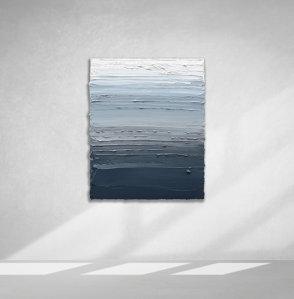 A dark grey blue, light blue, blue green, and white thickly textured abstract painting hanging on a white wall in natural light by Teodora Guererra.