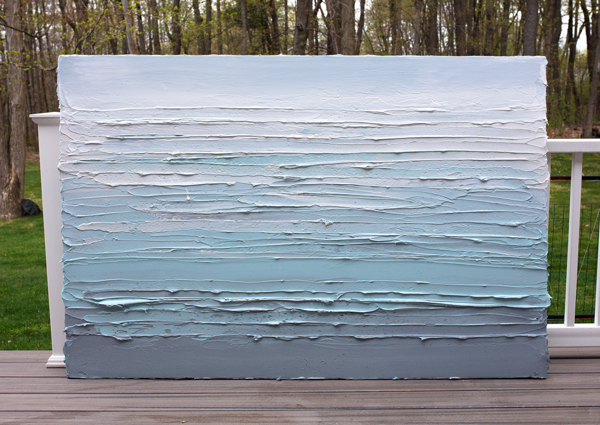 An abstract painting by Teo Guererra with turquoise impasto brushstrokes in a color gradient is sitting on a deck in the artists studio.