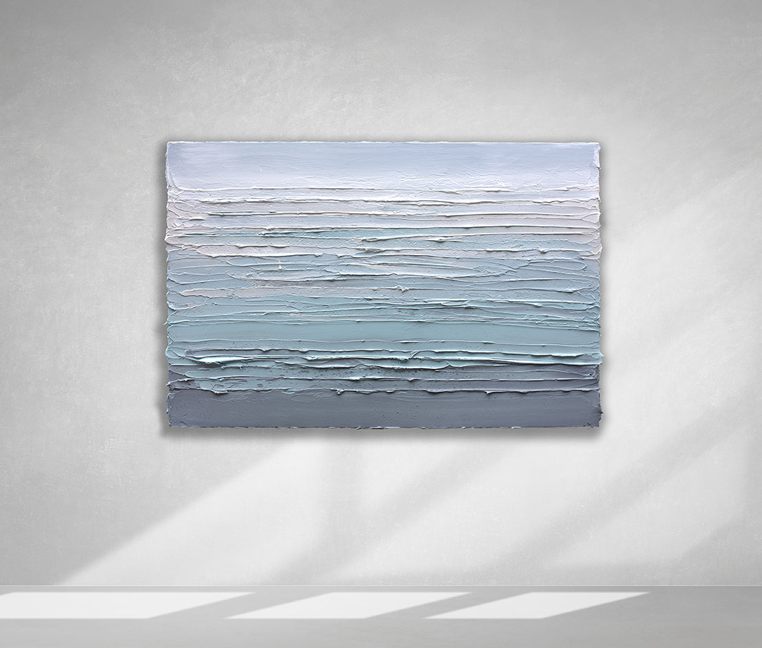 A white, teal and grey heavily textured abstract painting like sculpture by Teodora Guererra hangs on a white wall in natural light.