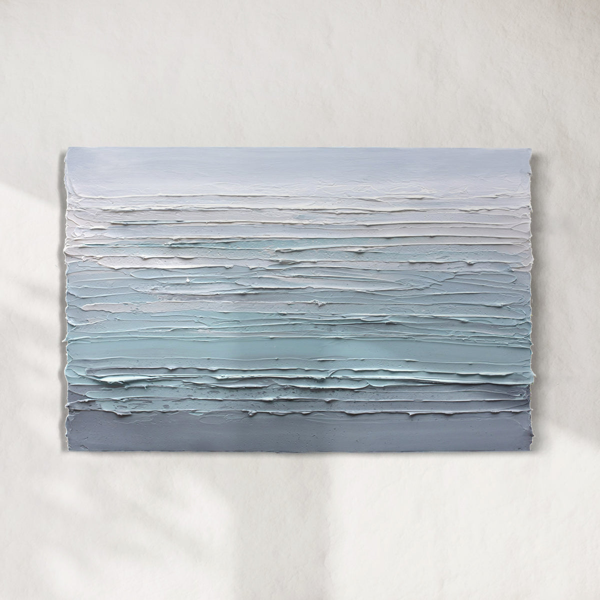 A white, teal and grey heavily textured abstract painting like sculpture by Teodora Guererra hangs on a white wall in natural light.