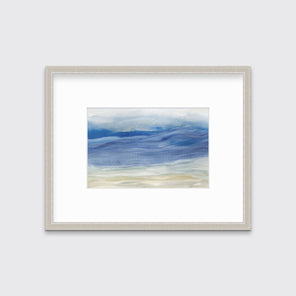 A blue, white and beige abstract print in a silver frame with a mat hangs on a white wall.