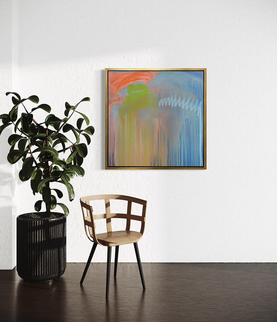 A blue, orange and green abstract print framed in a gold floater frame by Teodora Guererra hanging on a white wall with a large potted plant and chair in front.