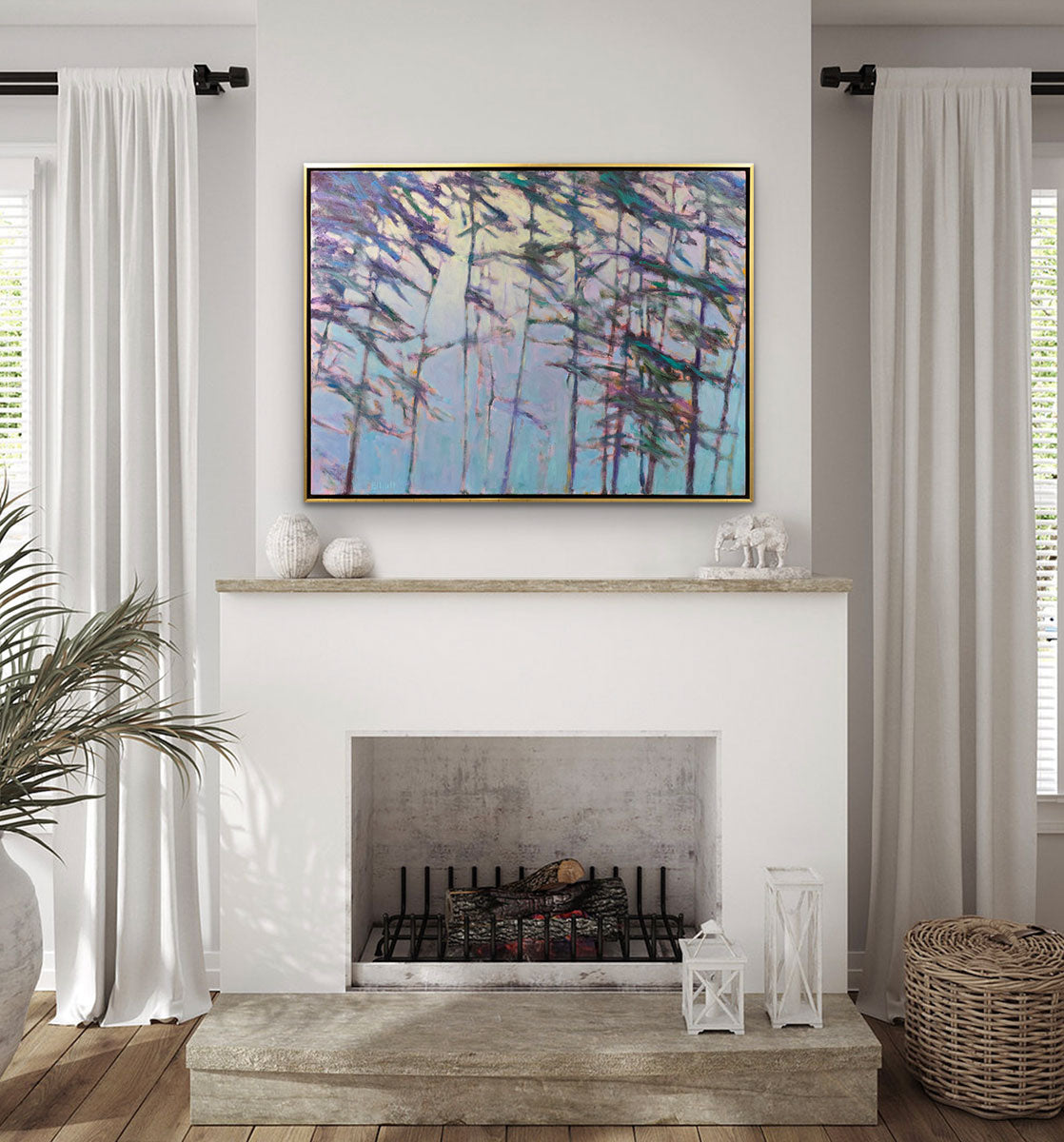 An impressionistic landscape painting by Ken Elliott of trees with blue and purple leaves in a gold floater frames hangs on a white wall above a fireplace. The fireplace is in between windows with white curtains. White decor sits on top of the natural wood mantle with a potted plant and wicker basket on either side of the fireplace.