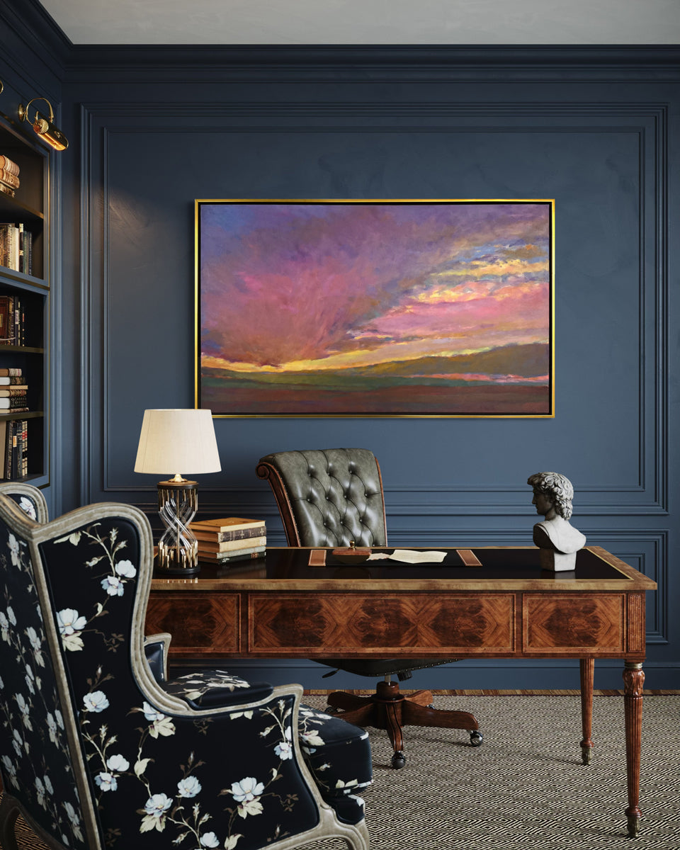 Decorative office with a wooden desk, floral armchair, and framed artwork on a blue wall.