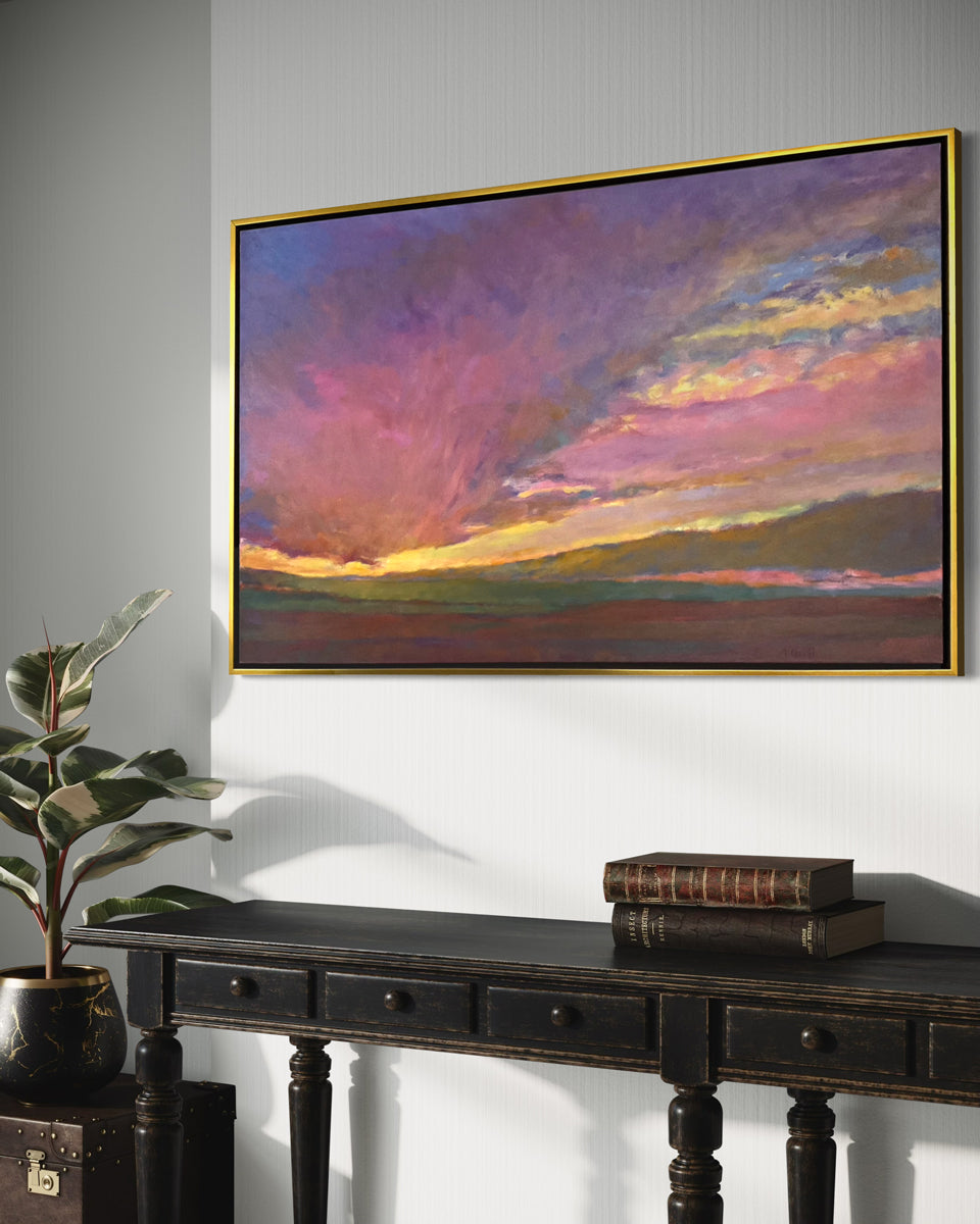 Framed artwork of a colorful sunset over a mountain landscape on a wall above a dark wooden console table.