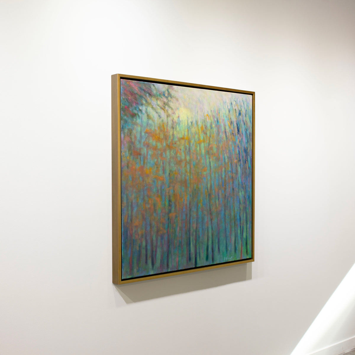 A colorful abstracted landscape painting framed in a gold frame hangs on a white wall.