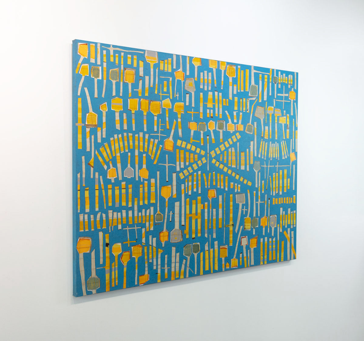An abstract panting of yellow sticks and "lollipops" on a blue background is seen at an angle on a gallery wall.