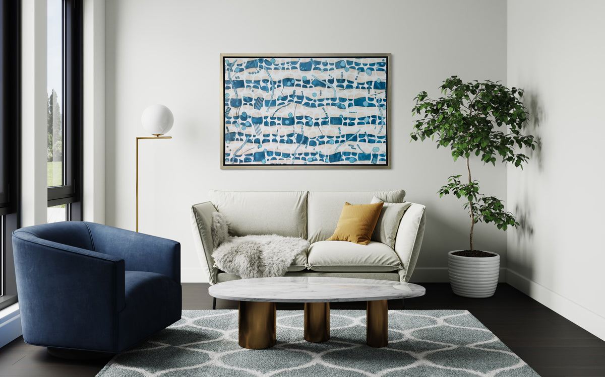 A blue, teal and beige geometric abstract print in a silver floater frame hangs on a white wall above a white loveseat sofa, a rounded blue armchair and a modern white marble coffee table.