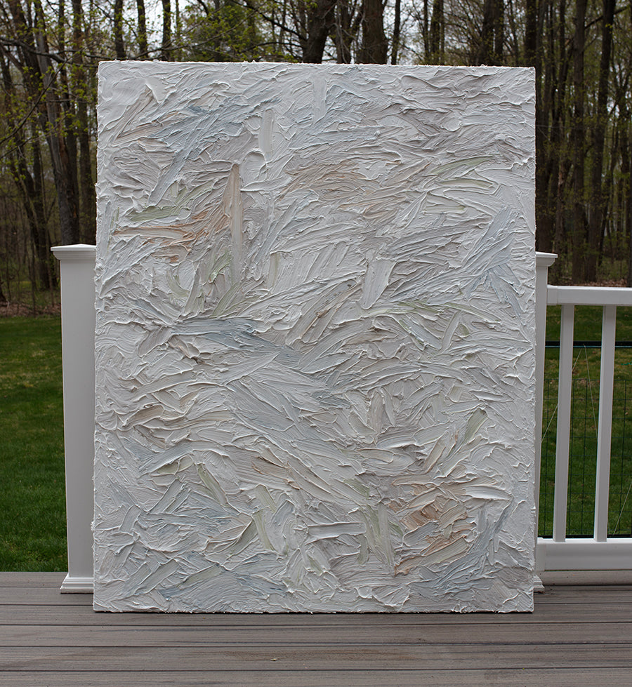 An abstract painting with thickly textured brushstrokes of beige, green, orange, and blue sitting on the artists deck.