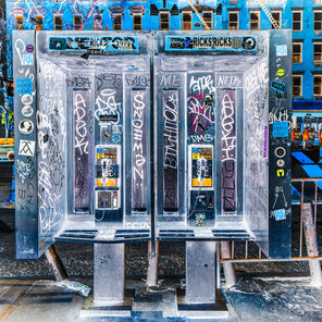 A contemporary photograph by Peter Mendelson of two phone booths covered in graffiti on a city street. 