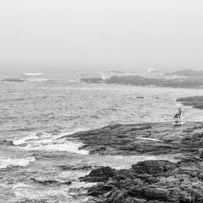 A black and white photograph of a lifeguard sitting on a rocky coast of Maine. 