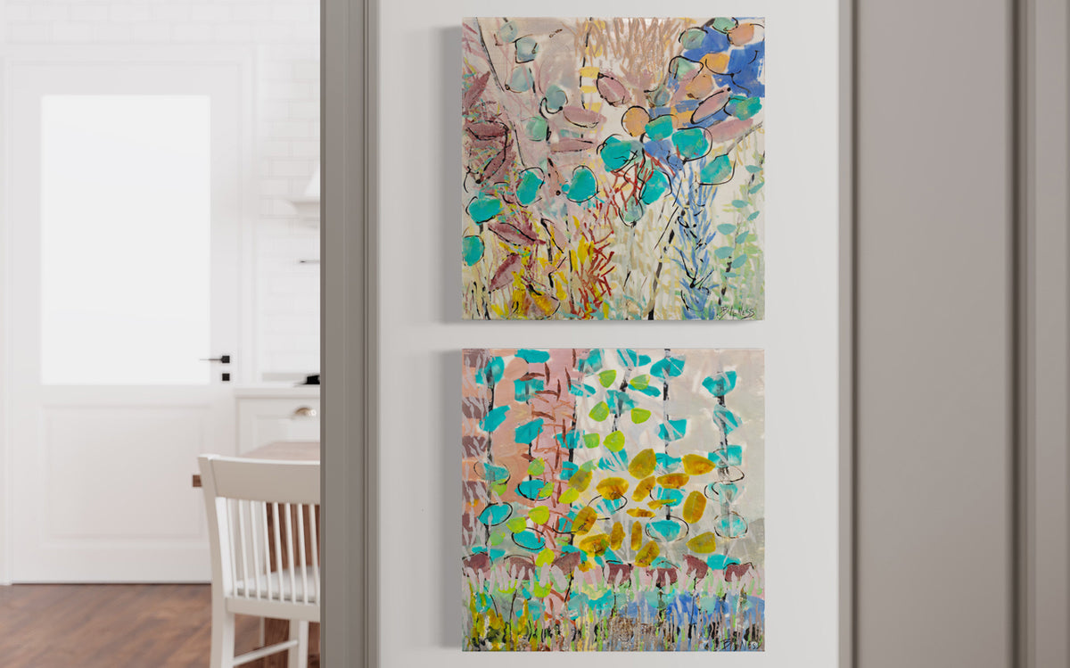 Two abstract colorful paintings hang stacked one above the other on a white wall in a hallway entering a room with a table and door. 