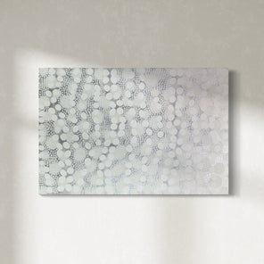 A white, grey, and silver abstract painting hangs on a sunny wall.