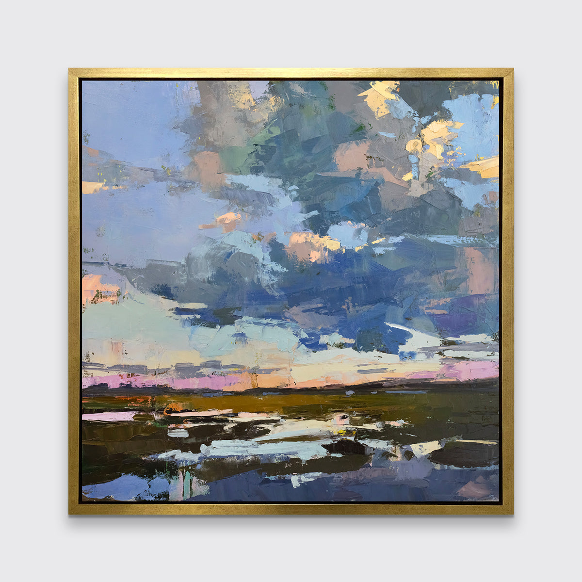 A blue coastal landscape art print framed in a gold frame hangs on a white wall.