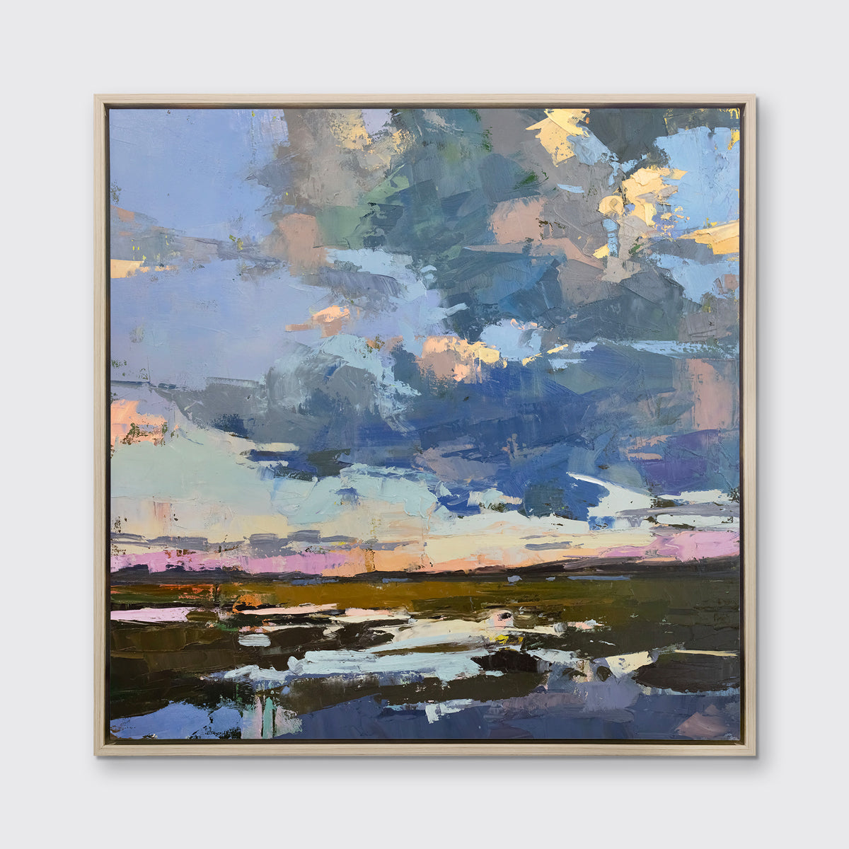 A blue coastal landscape art print framed in a white oak frame hangs on a white wall.