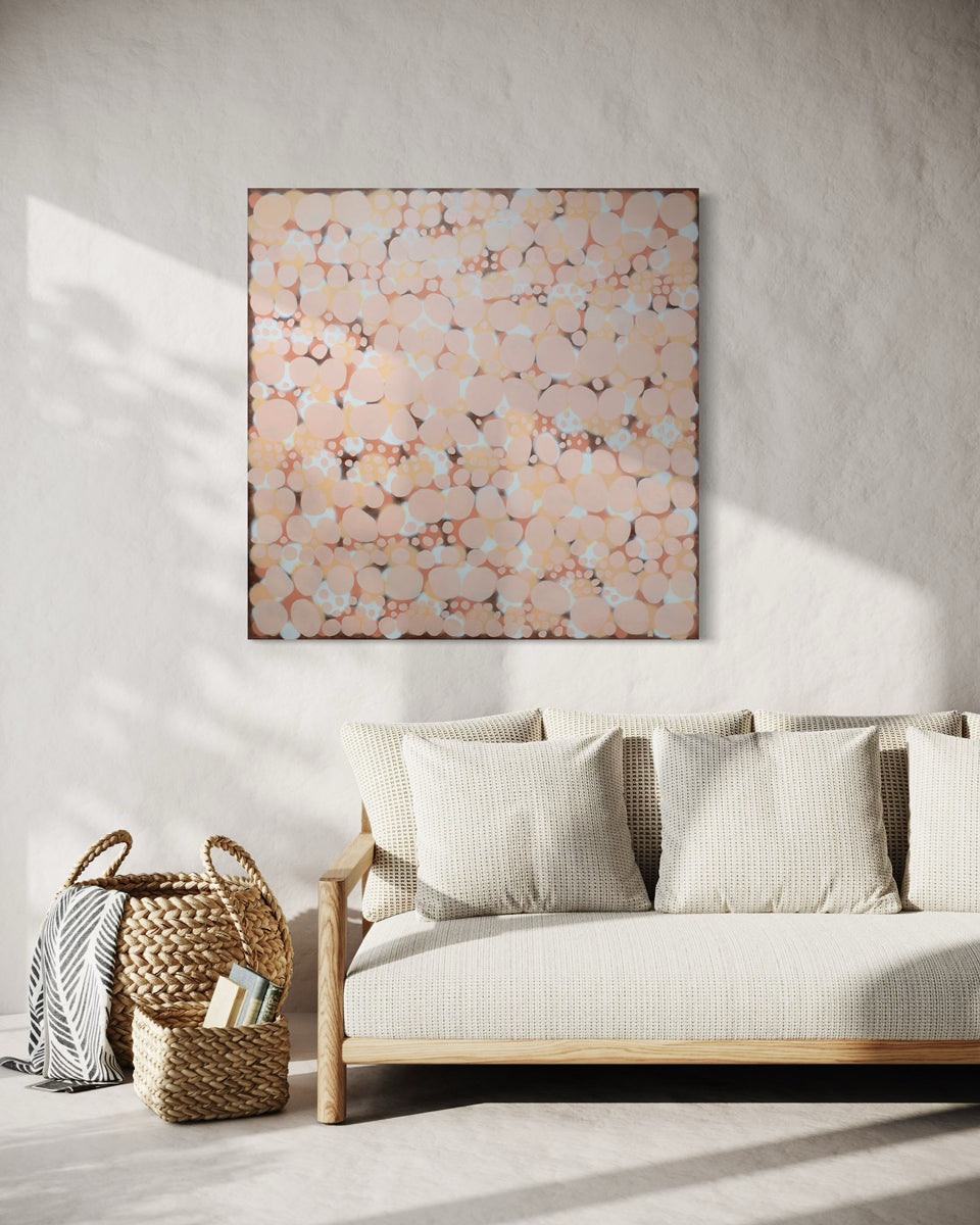 An orange, salmon, coral and pink abstract painting hangs on a white wall above a cream sofa with baskets to the side.