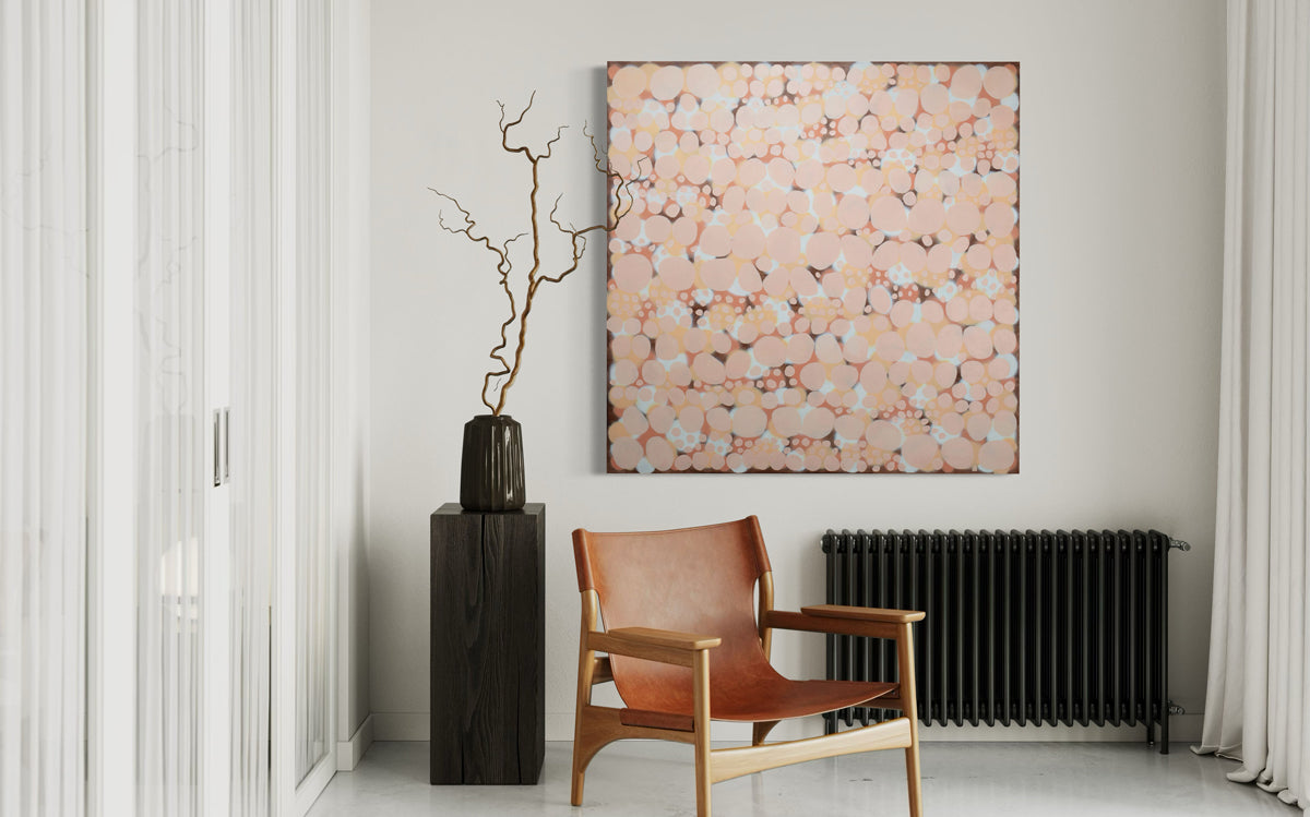 An orange, salmon, coral and pink abstract painting hangs on a white wall above a black radiator with an orange leather chair.