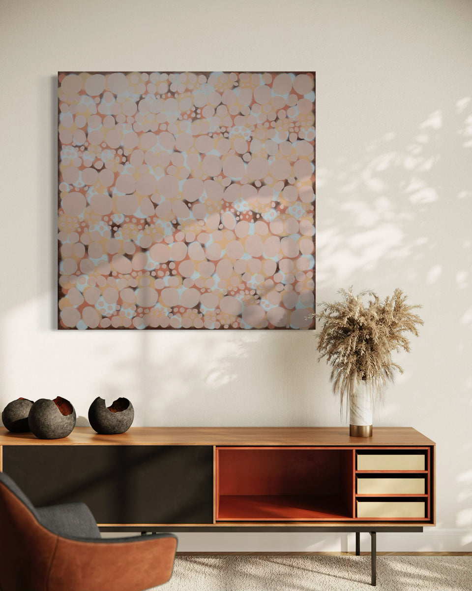 An orange, salmon, coral and pink abstract painting hangs on a white wall above a low wood credenza.