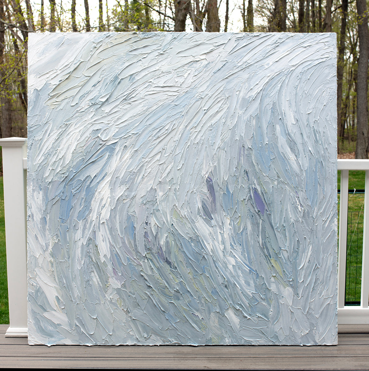 A Grey blue, light blue, lavender, celadon and white thickly textured abstract painting leaning on a deck outside in natural light by Teodora Guererra.