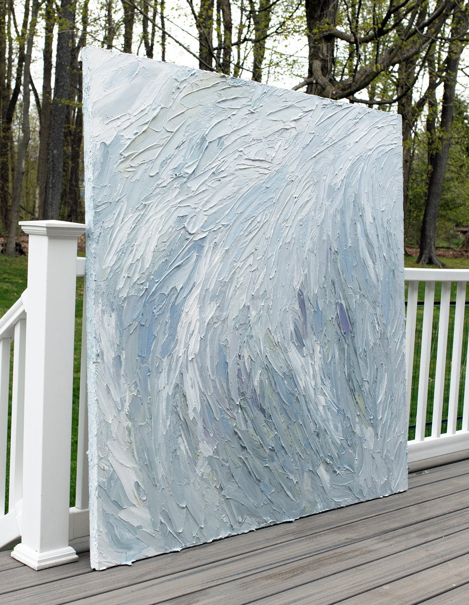 A Grey blue, light blue, lavender, celadon and white thickly textured abstract painting leaning on a deck outside in natural light by Teodora Guererra.