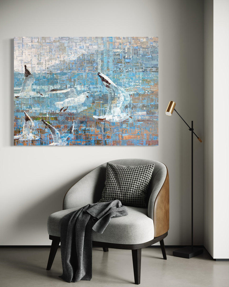 A painting on recycled metal print plates depicting seagulls in flight is hung over a grey chair.