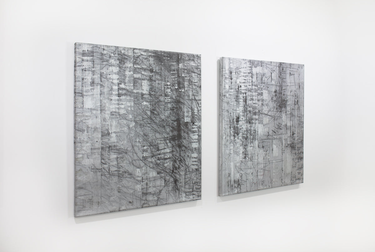 Two black and silver abstract paintings hang on a white wall.