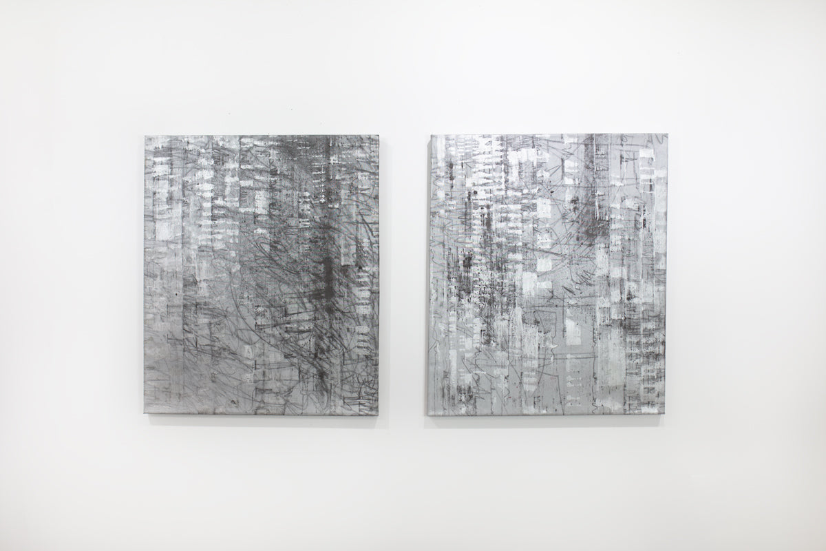 Two black and silver abstract paintings hang on a white wall. 