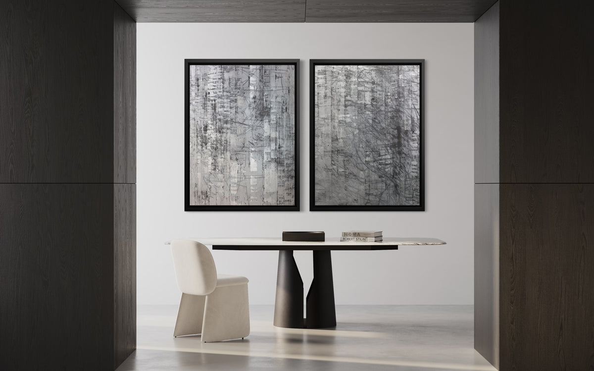 Two abstract silver-grey limited edition art prints by Ned Martin in black frames hang side-by-side on a white wall with a black and white modular table and white chair in front of it.