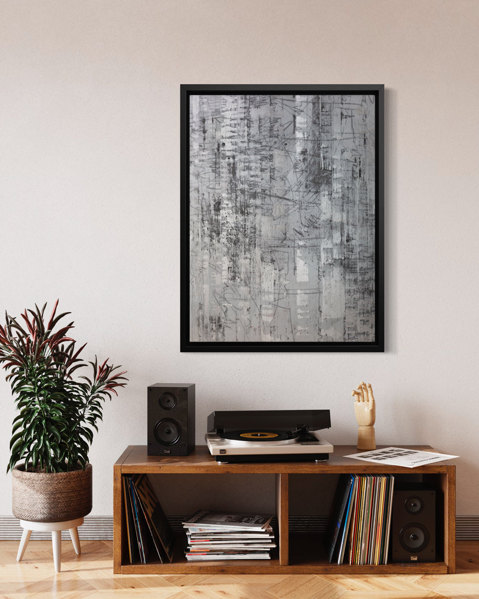 An abstract silver-grey limited edition art print by Ned Martin in a black frame hangs on a white wall in a room with a stereo console and a potted plant.
