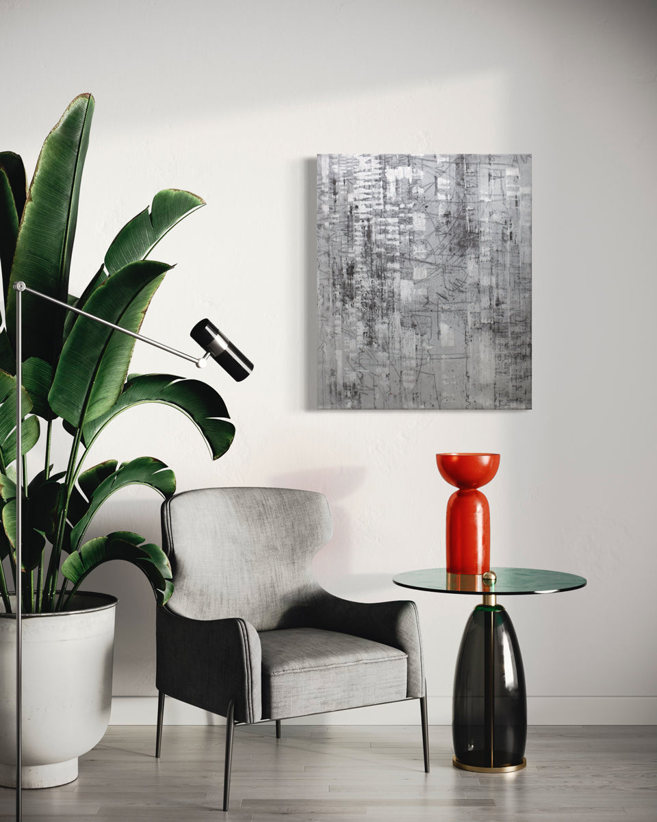 A black and silver abstract painting hangs on a white wall above a modern grey armchair, large floor plant, and modern end table with a red sculpture. 