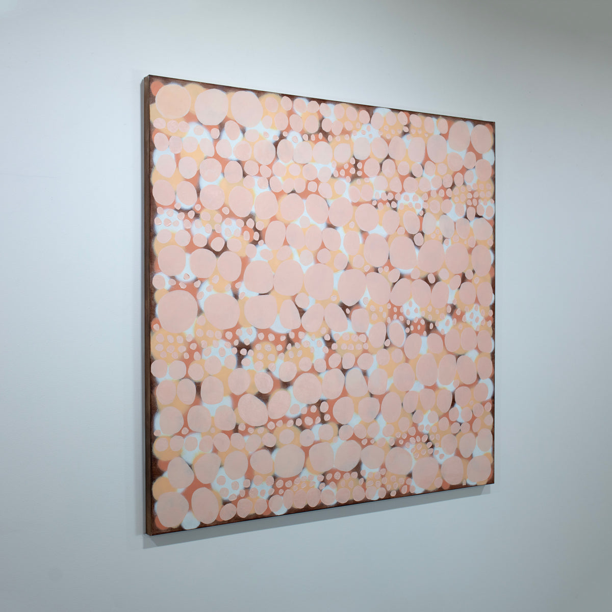 An orange, salmon, coral and pink abstract painting hangs on an angle on a white wall. 