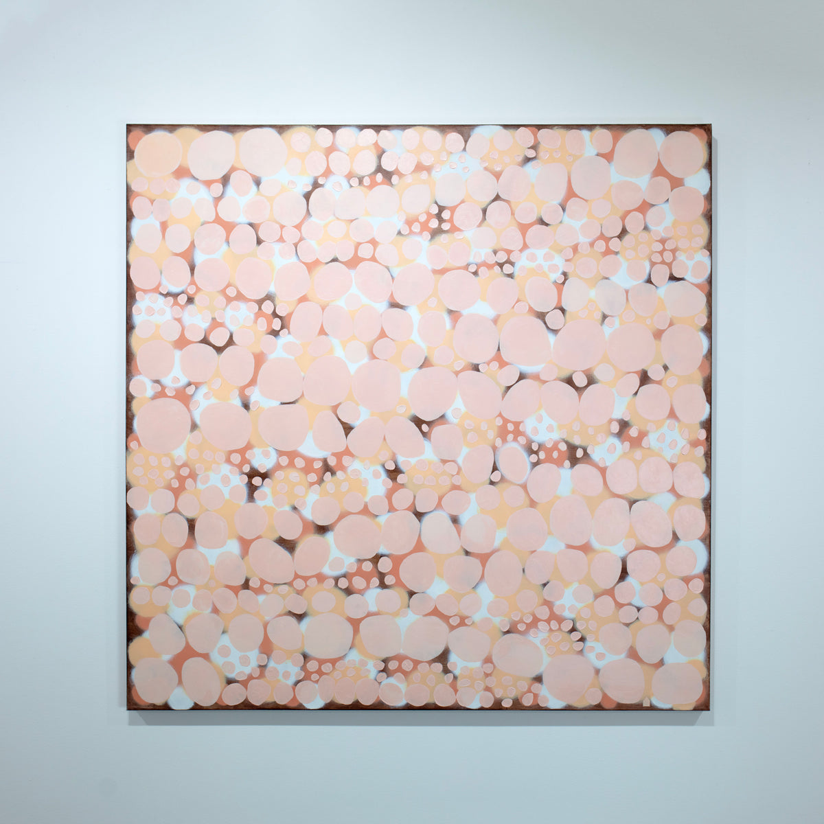 An orange, salmon, coral and pink abstract painting hangs on a white wall. 