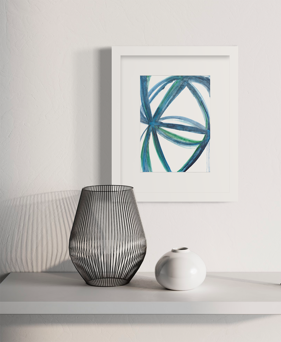 A blue, green and white abstract print in a white frame with a mat hangs on a white wall above a white surface with a black wire vase and a small rounded white vase.